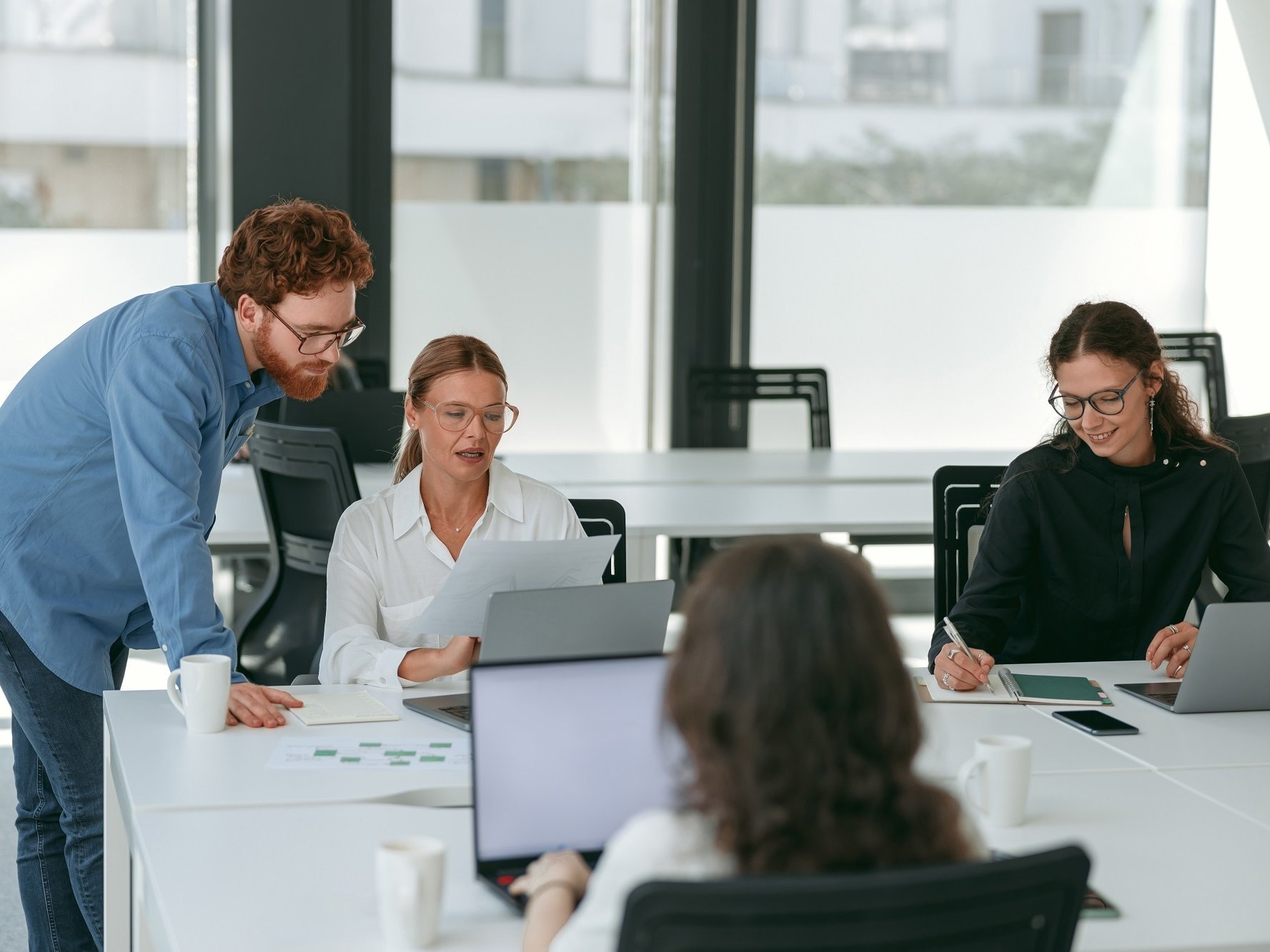 Vier Personen sitzen mit Laptops in einem Co-Working Space. Zwei davon unterhalten sich über etwas, dass auf dem Laptop angezeigt wird.