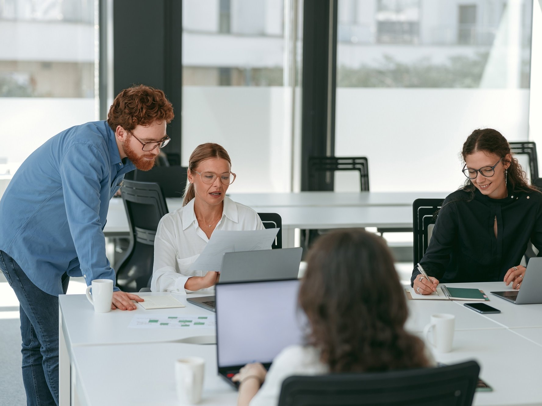 Vier Personen sitzen mit Laptops in einem Co-Working Space. Zwei davon unterhalten sich über etwas, dass auf dem Laptop angezeigt wird.