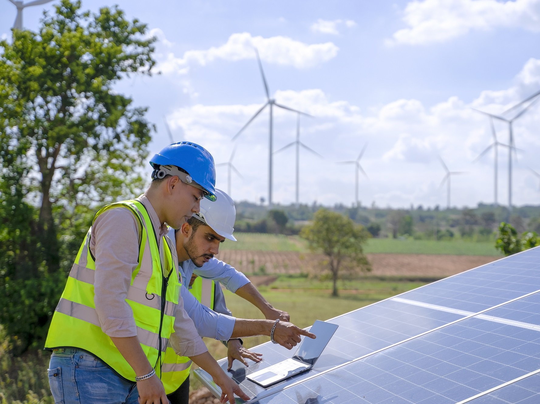 Zwei Bauarbeiter stehen an Photovoltaikanlage. Im Hintergrund Windräder in der Umwelt.