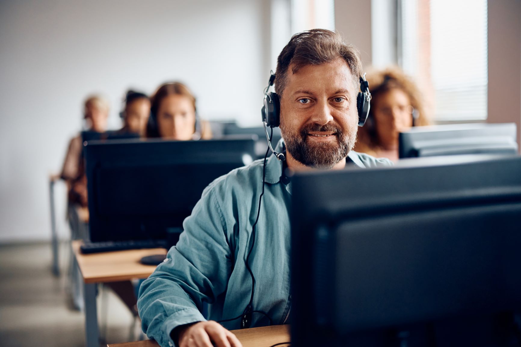 Ein Mann mittleren Alters trägt ein Headset und nimmt an einer Online Weiterbildung teil. 