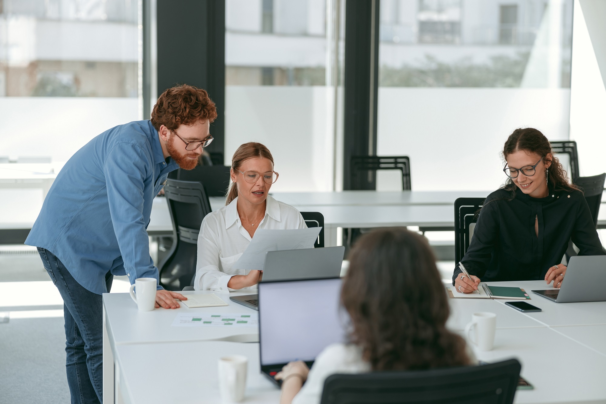 Vier Personen sitzen mit Laptops in einem Co-Working Space. Zwei davon unterhalten sich über etwas, dass auf dem Laptop angezeigt wird.