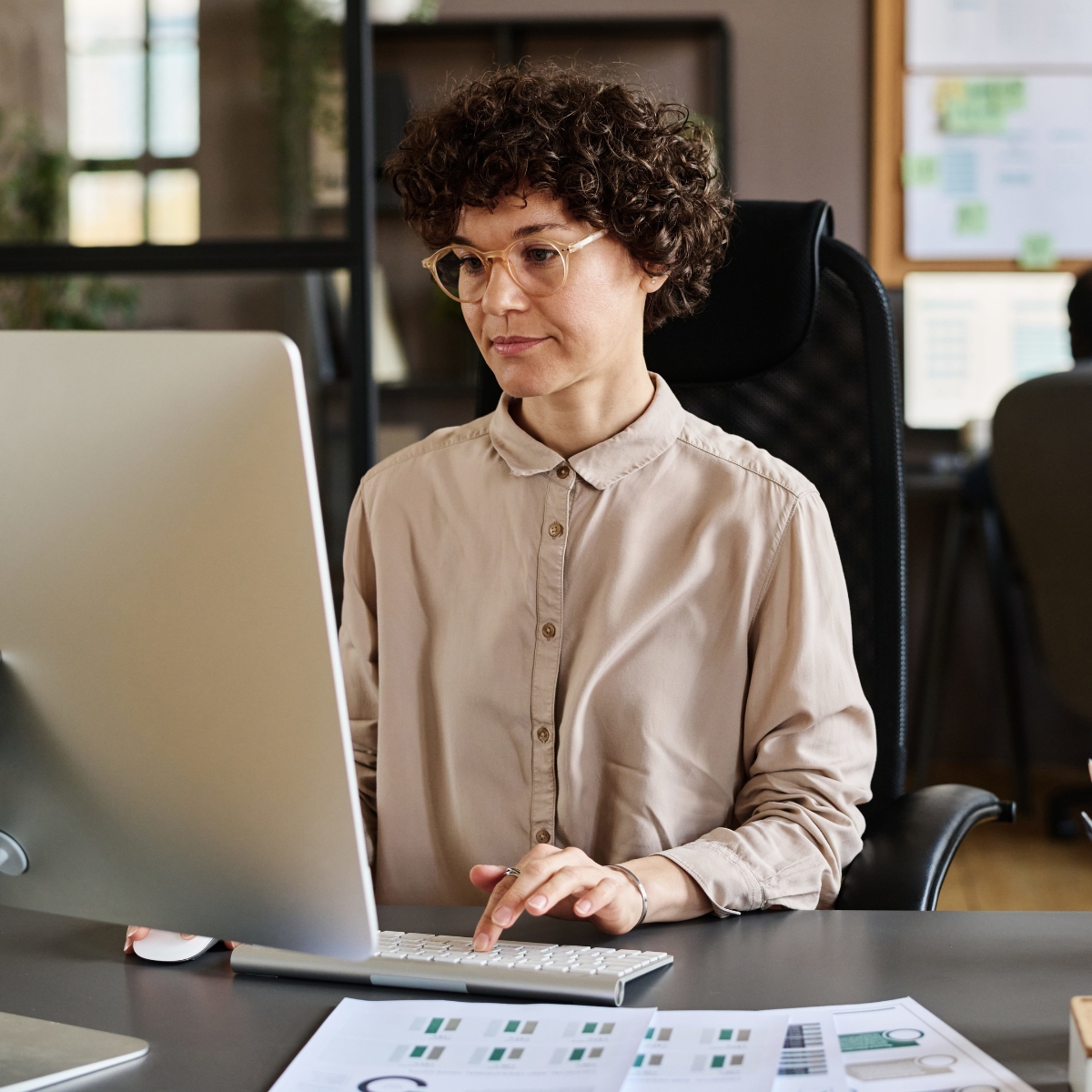 Eine Frau mit kurzen Haaren sitzt am Schreibtisch und arbeitet am Computer