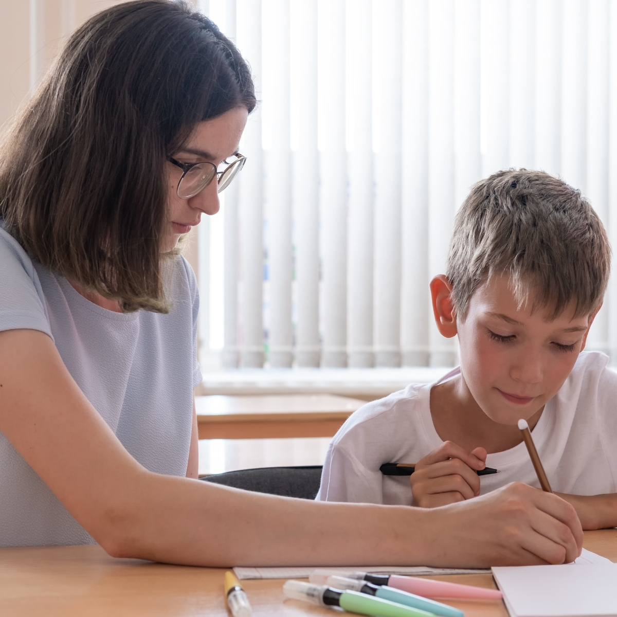 Eine Frau und ein Junge sitzen an einem Tisch. Sie bearbeiten gemeinsam ein Arbeitsblatt.