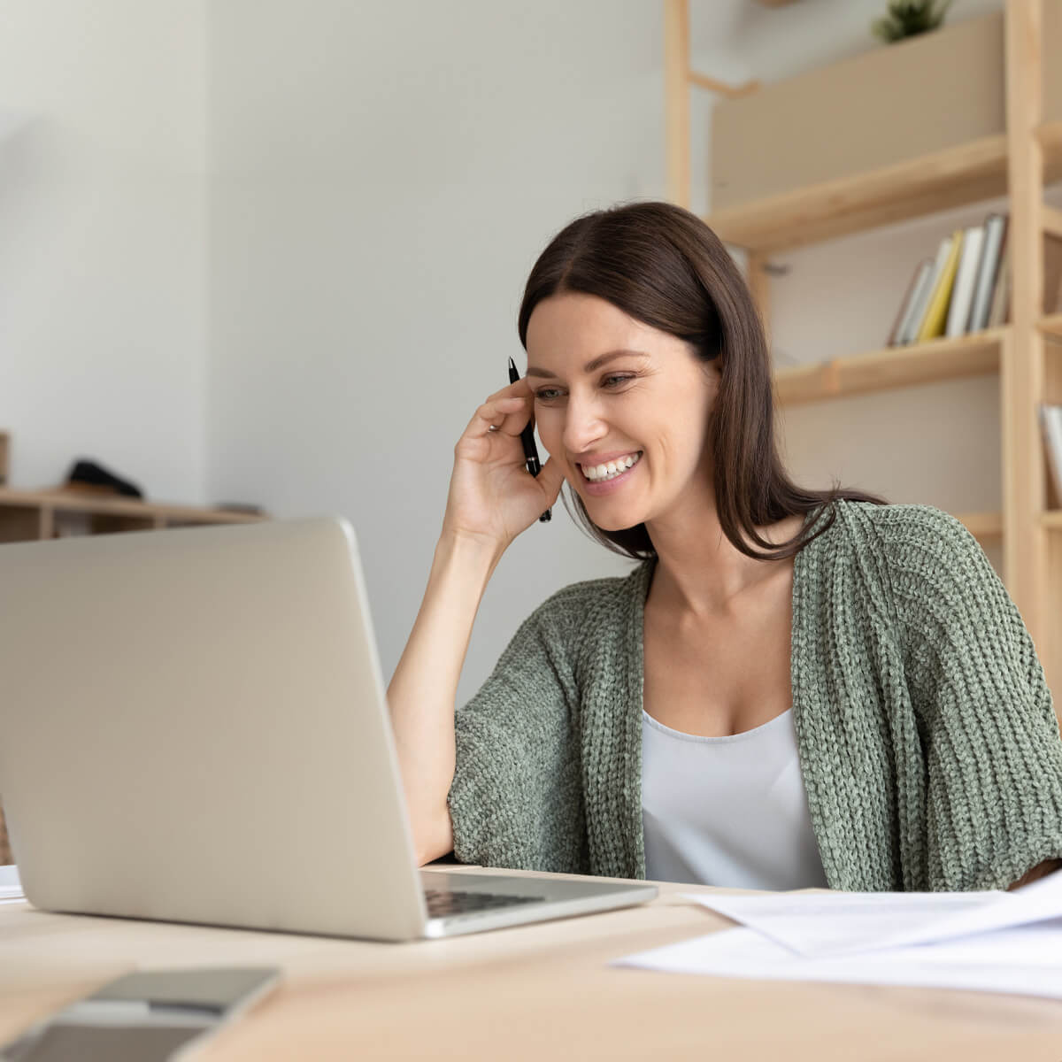 Weiterbildungen Eine Frau mit Stift in der Hand blickt lächelnd in ihren Laptop.